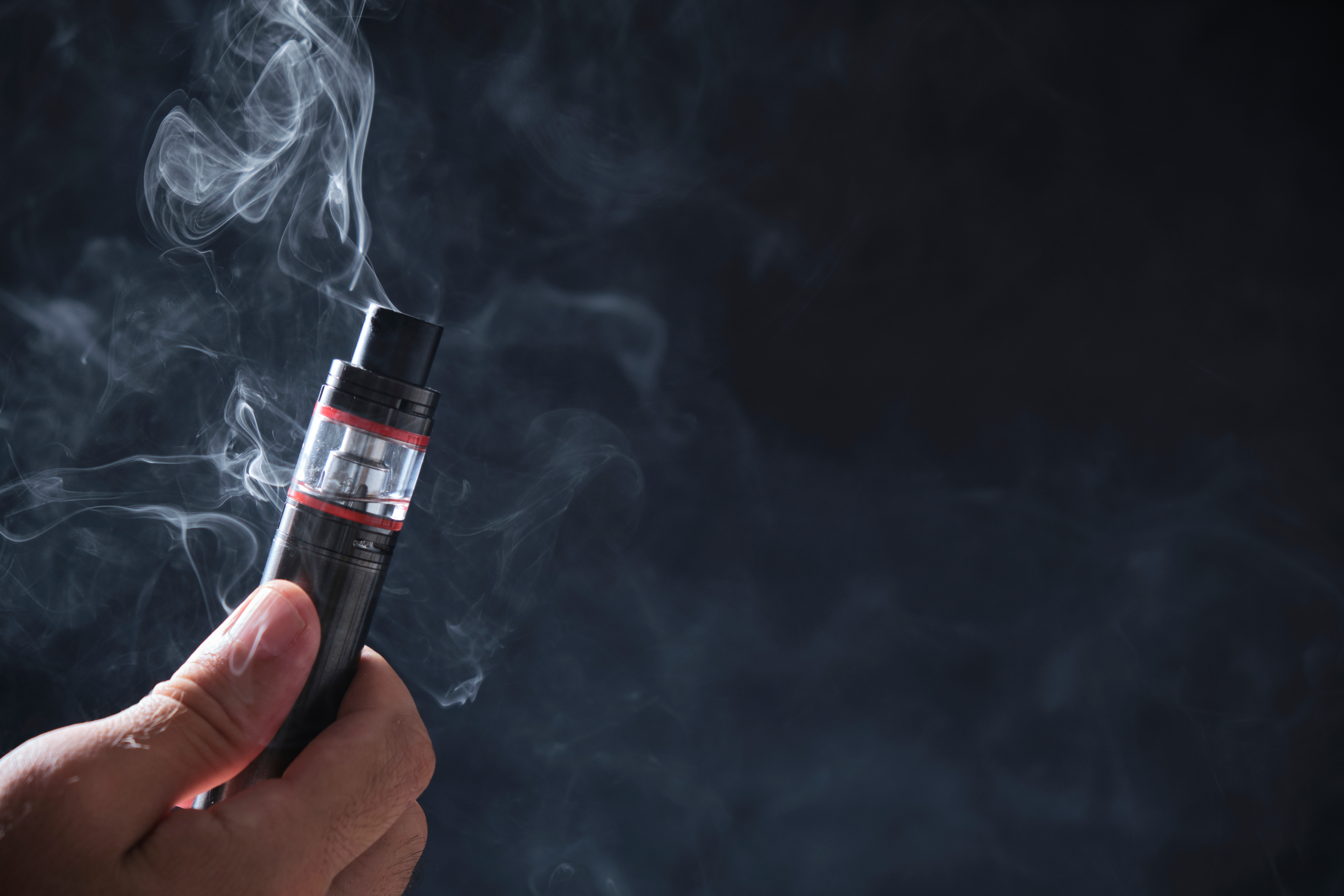 Person holding a vaping device with visible vapor against dark background