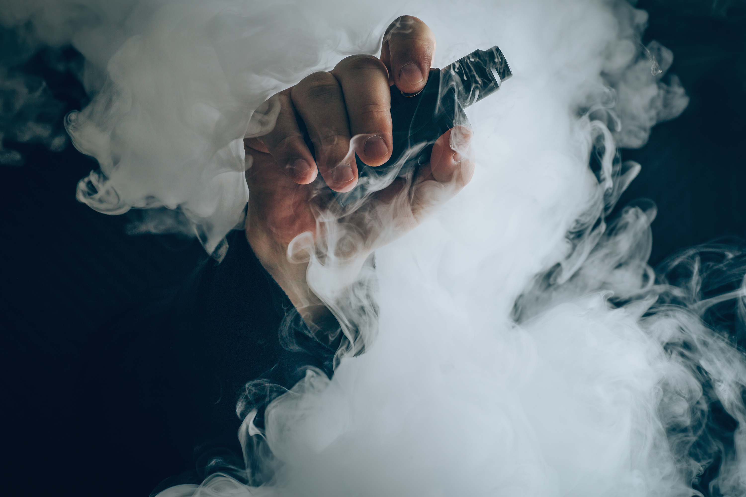 Hand holding vaping device with white vapor cloud against dark background