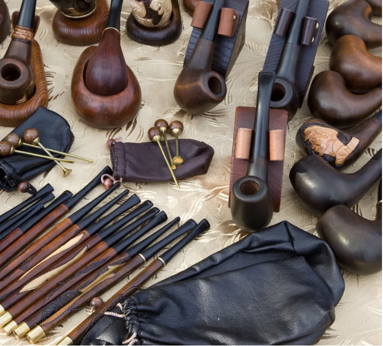 Collection of wooden smoking pipes and tobacco accessories displayed on cream fabric