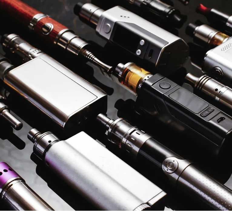 Collection of vaping devices and e-cigarettes arranged in rows on reflective surface